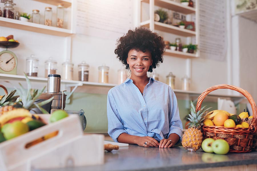 Business Insurance - Small Business Owner Stands at the Counter of Her Restaurant, Baskets of Fruit and Canisters of Toppings Around Her