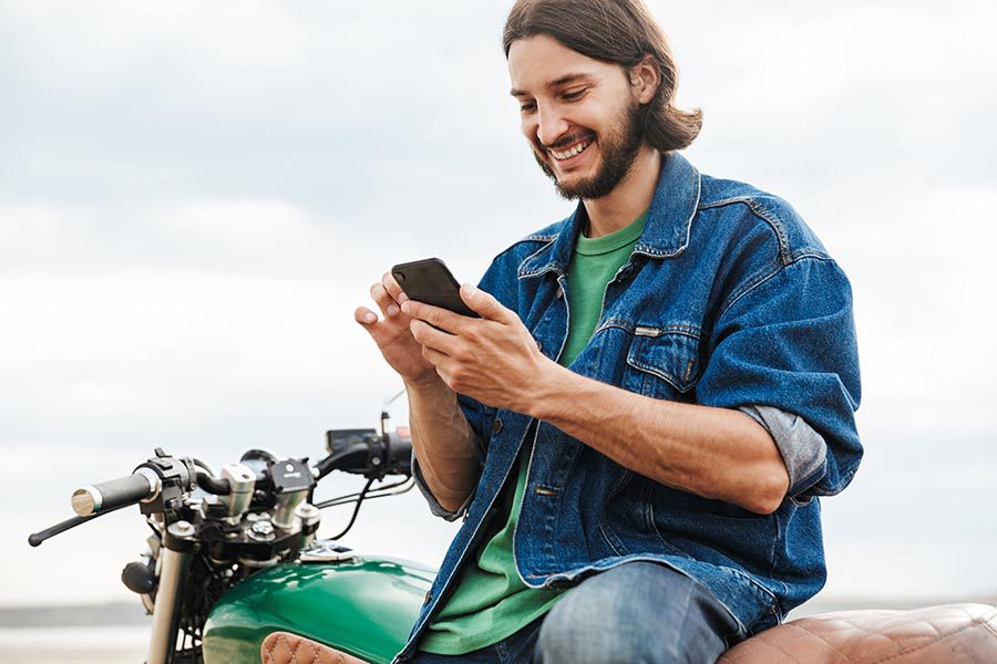 Client Center - Young Man in a Denim Jacket Uses a Phone While Leaning Against His Motorcycle