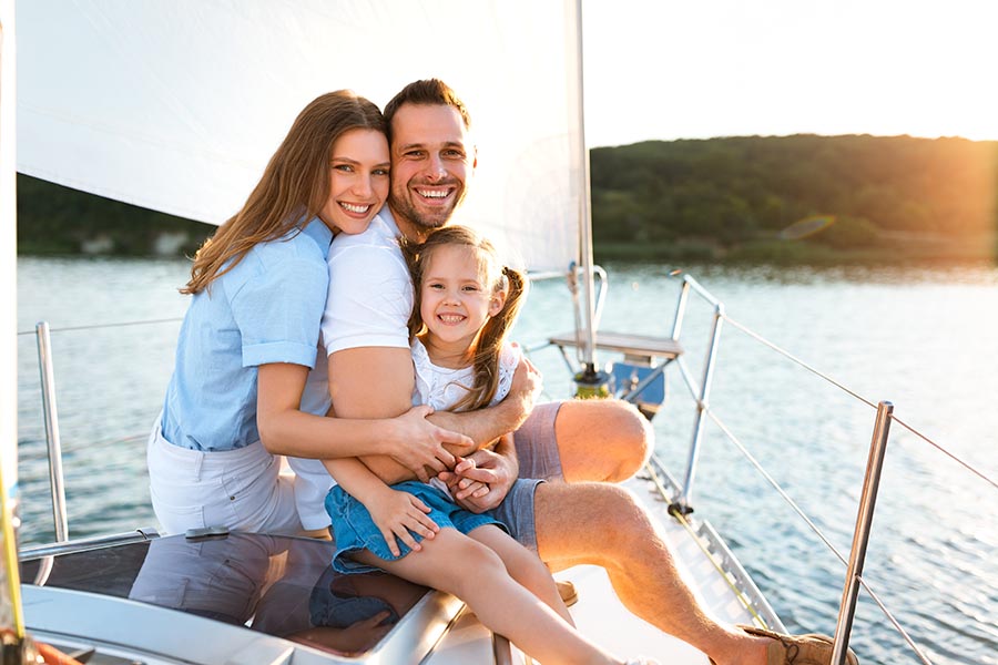 Personal Insurance - Mother, Father and Daughter Hug on a Sailboat With the Sun Shining on Them